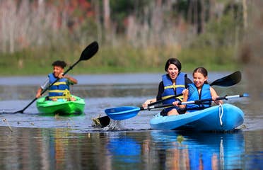 Featured Contributor, Clarissa Laskey (middle), kayaks with her daughter (right) in a blue kayak while her son (left) kayaks in his own green kayak.