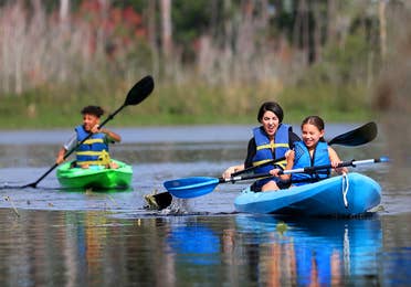 Featured Contributor, Clarissa Laskey (middle), kayaks with her daughter (right) in a blue kayak while her son (left) kayaks in his own green kayak.