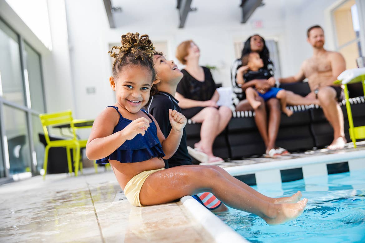 Featured author, Sally Butan of @butanclan, children dip their feet into the pool as her daughter looks at the camera wearing a swimsuit.