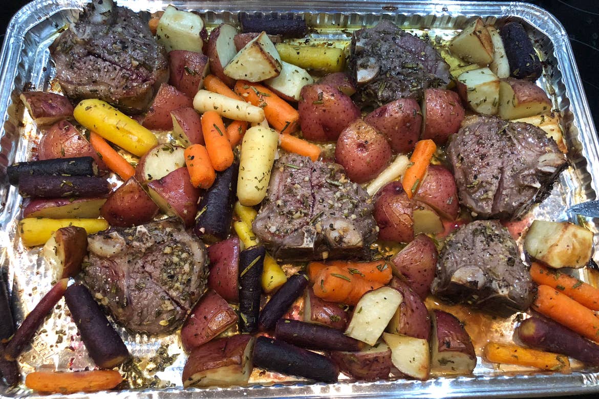 A disposable aluminum tray filled with roasted carrots, potatoes and beef.