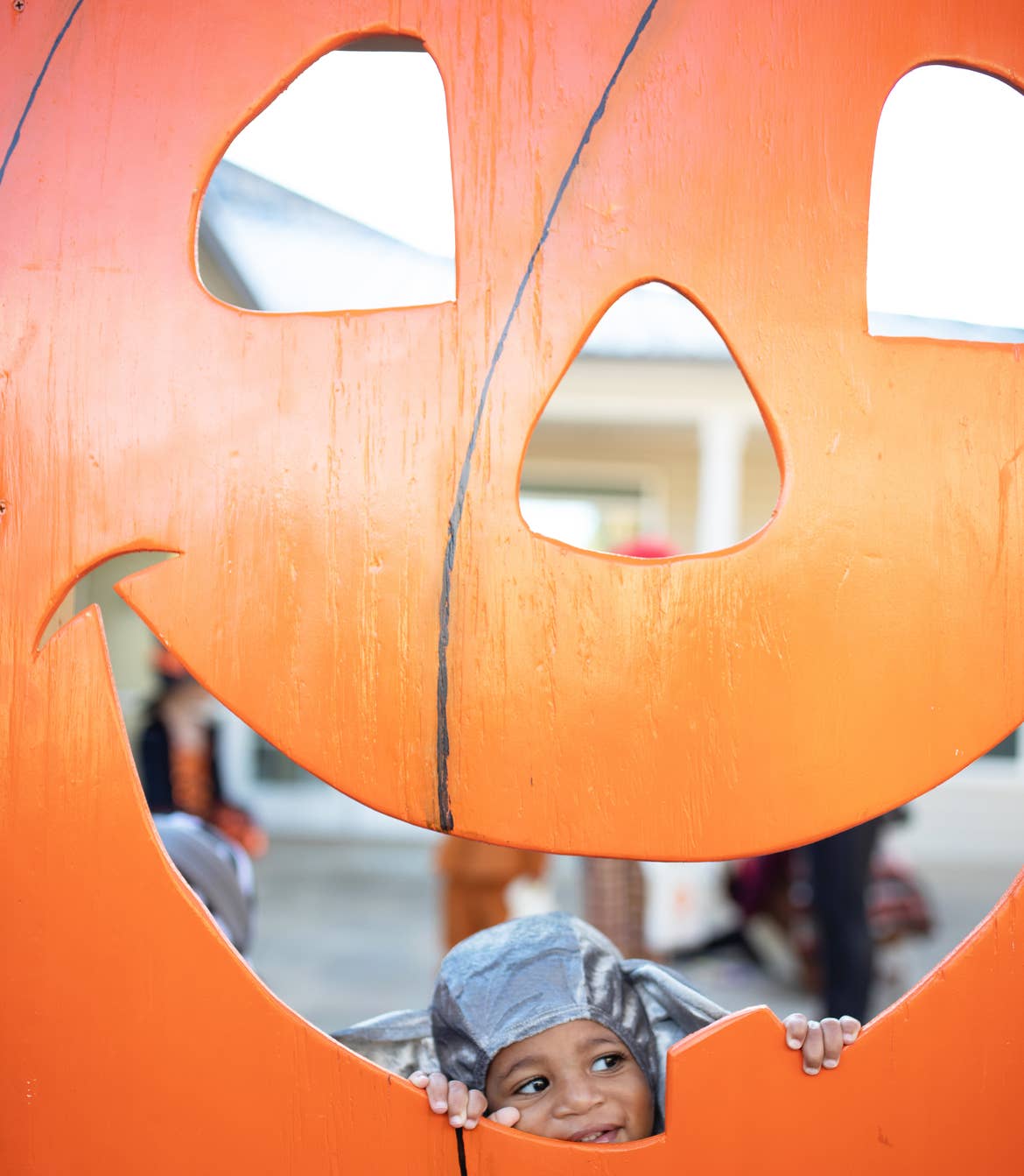Tina's son in costume peeking through a giant pumpkin cut-out decoration at Falladays at Villages Resort.