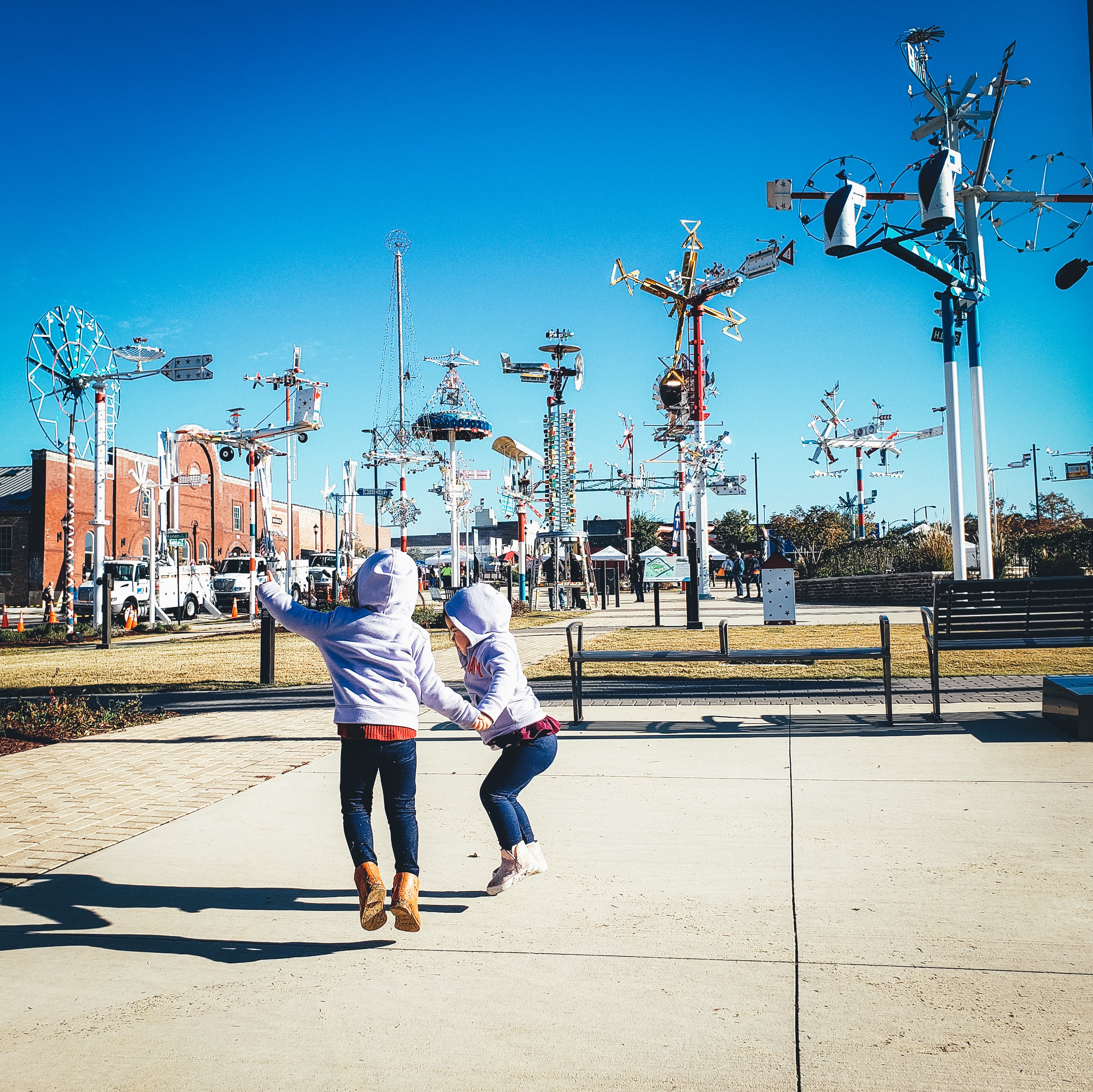 Angelica's kids jumping together in front of the whirligigs at Whirligig Park in Wilson, North Carolina.