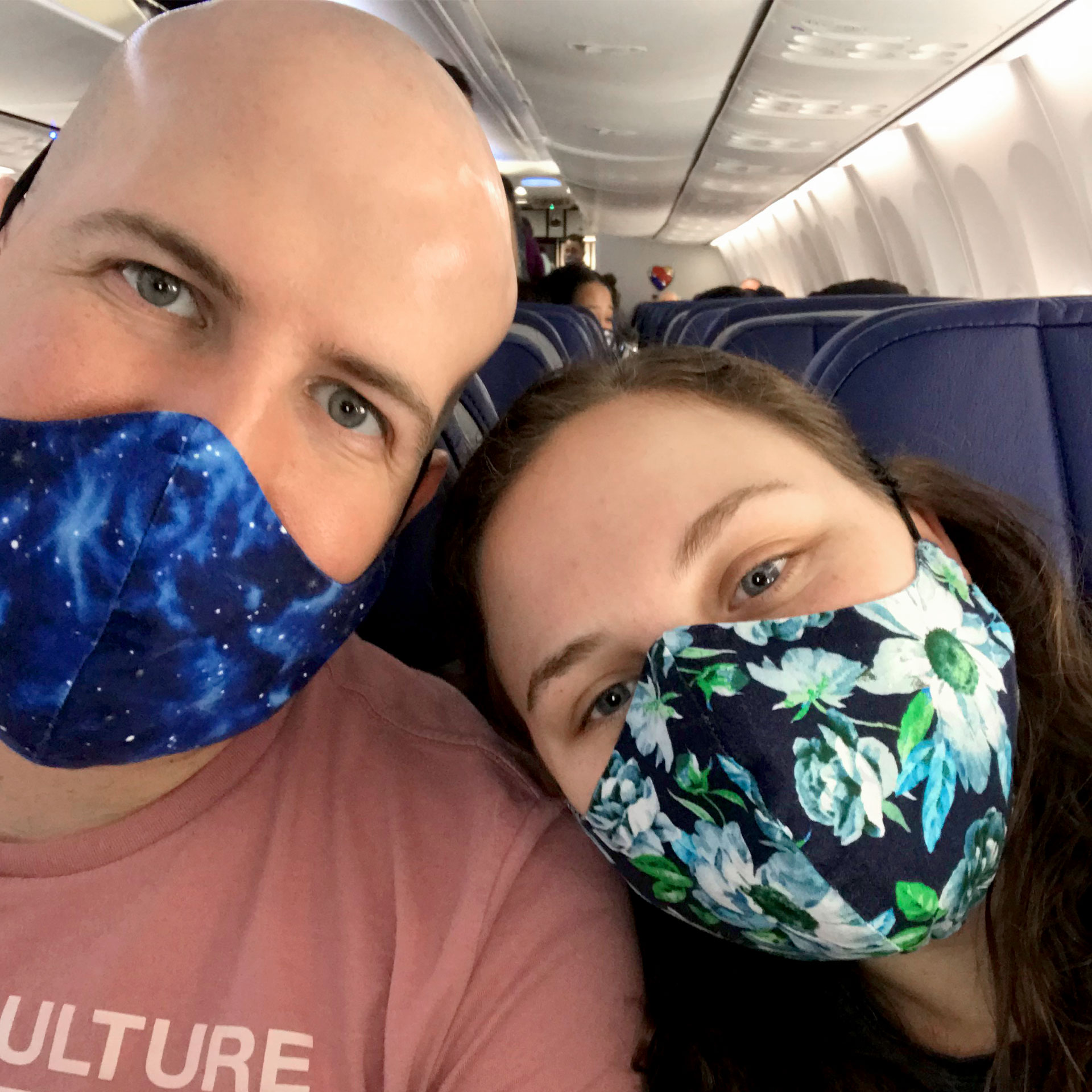 Featured Contributor, Ashley Fraboni (right) and her fiancé, Nicholas (left), sit on an airplane wearing face masks.