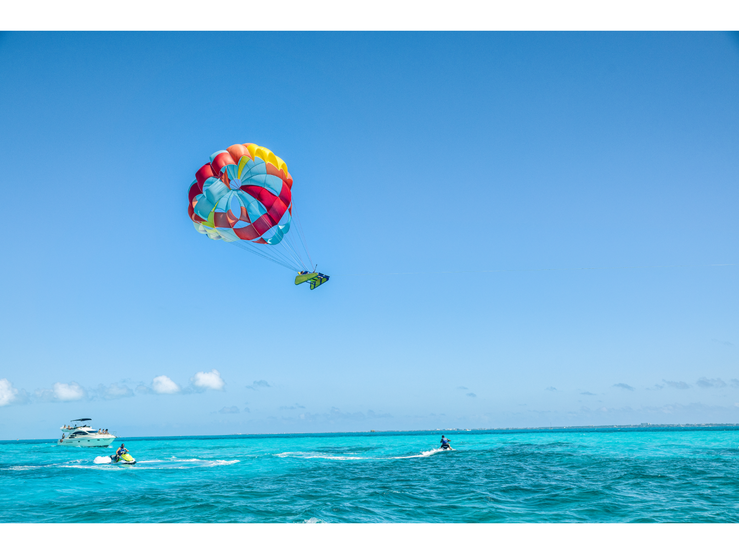 Colorful parasailing adventure over bright turquoise ocean waters, with a boat and jet skis nearby.