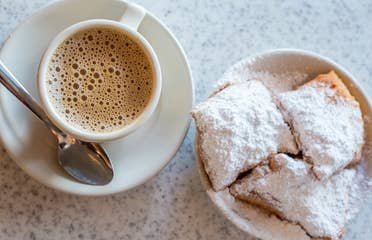 Beignets placed on a table with some coffee on white plates.