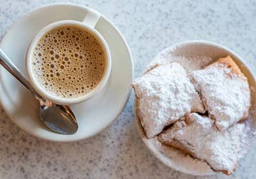 Beignets placed on a table with some coffee on white plates.