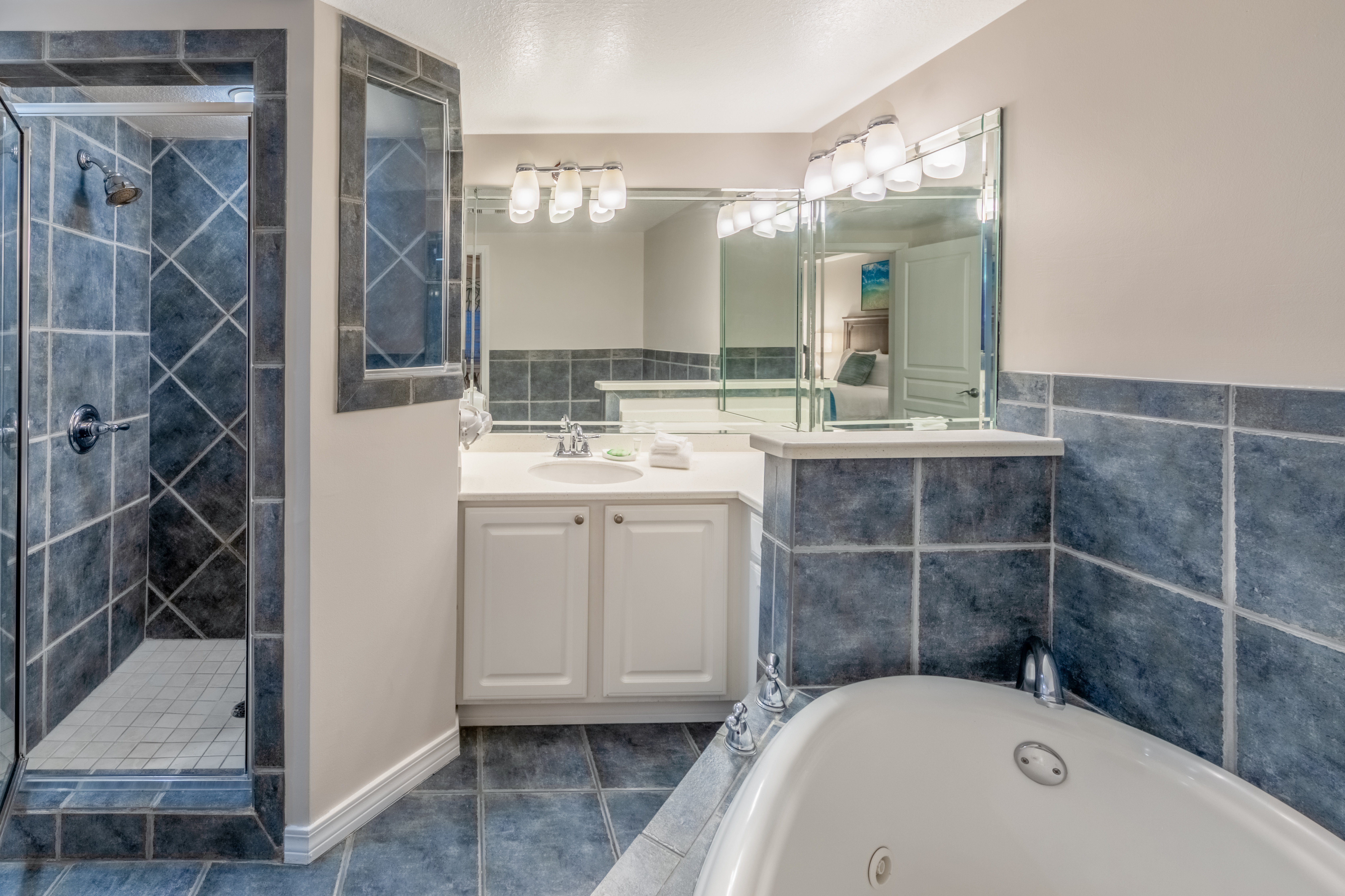Bathroom with whirlpool tub, walk-in shower, and sink with large mirror in a two-bedroom villa at Panama City Beach Resort