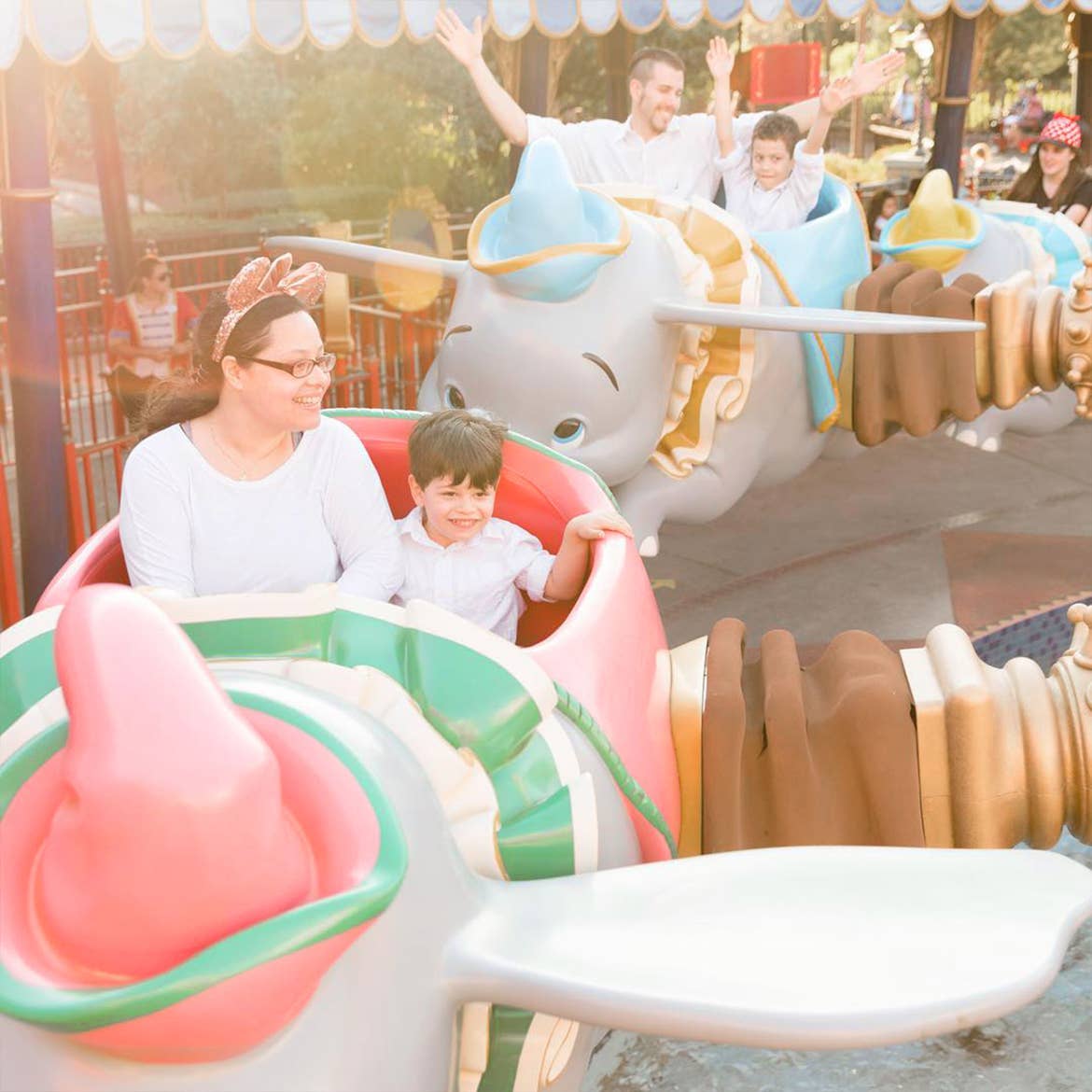 A woman, man and two young boys wear white shirts while riding a flying elephant ride.