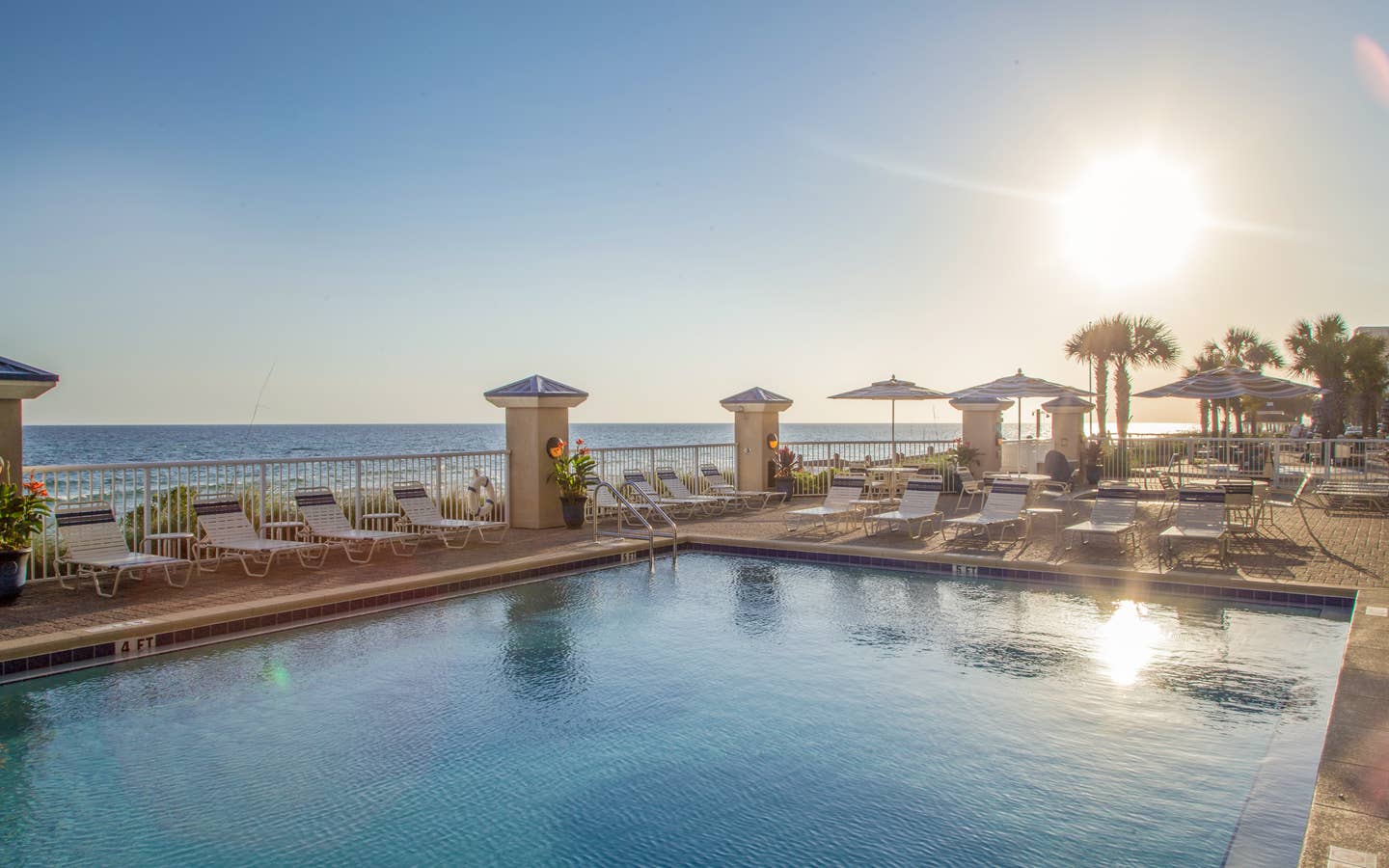 Outdoor pool with beach chairs surrounded by palm trees at Panama City Beach Resort