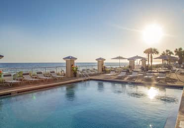 Outdoor pool with beach chairs surrounded by palm trees at Panama City Beach Resort
