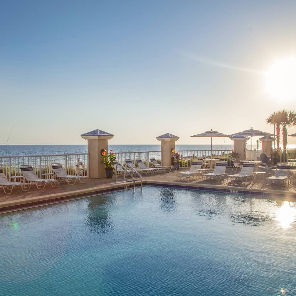Outdoor pool with beach chairs surrounded by palm trees at Panama City Beach Resort