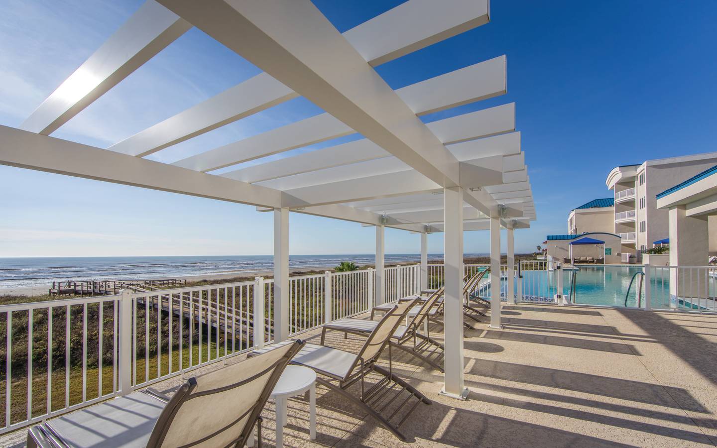 Beach chairs near a pool sitting under a pergola at Galveston Seaside Resort