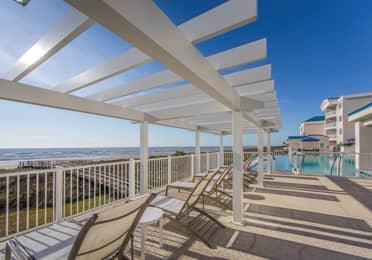 Beach chairs near a pool sitting under a pergola at Galveston Seaside Resort