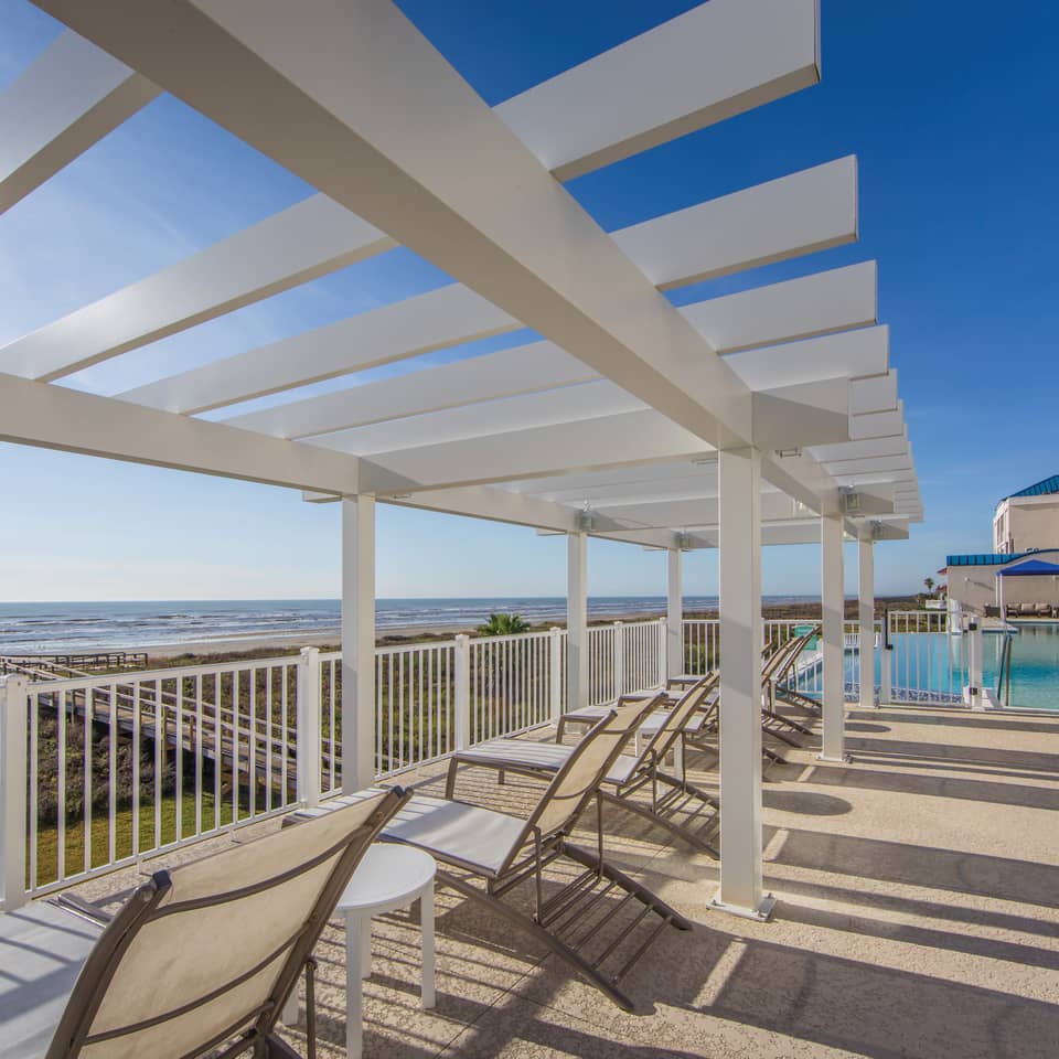 Beach chairs near a pool sitting under a pergola at Galveston Seaside Resort
