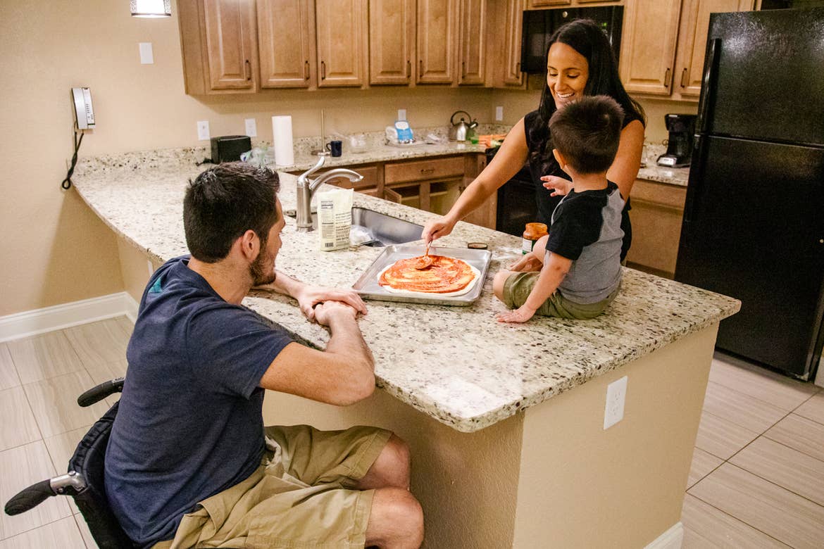 A man in a wheelchair, a woman and a toddler make a pizza in an ADA compliant villa.