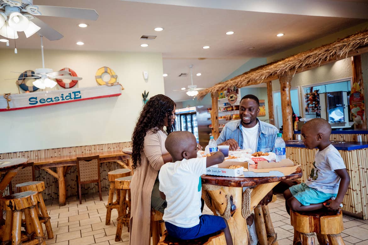 A woman, a man and two young boys enjoy pizzas at an indoor restaurant.