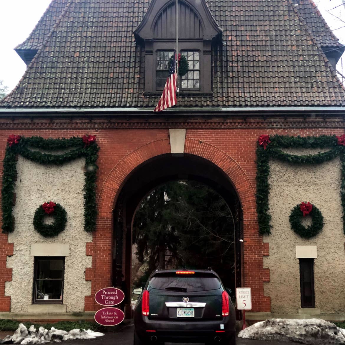 The exterior of the Biltmore Estate entrance under a cloudy sky with lush green garland decorating the facade as a black SUV enters.