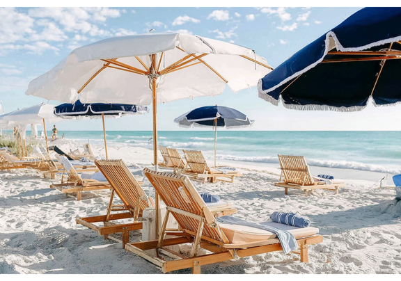 Boutique umbrellas and wooden beach chairs sit unoccupied on sandy bright beach.
