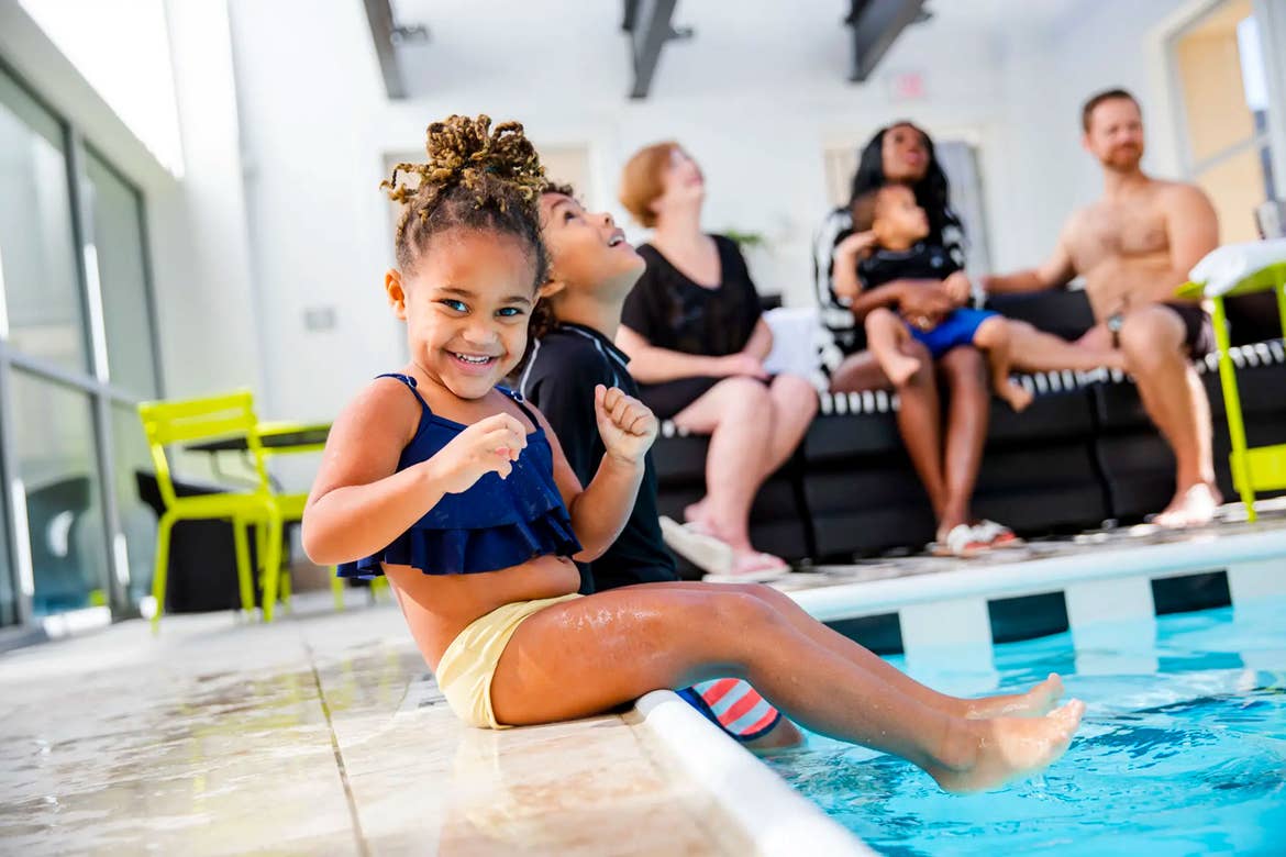 Featured author, Sally Butan of @butanclan, children dip their feet into the pool as her daughter looks at the camera wearing a swimsuit.