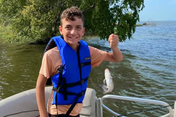 A caucasian boy wears a lifejacket on a pontoon holding a fish he caught.