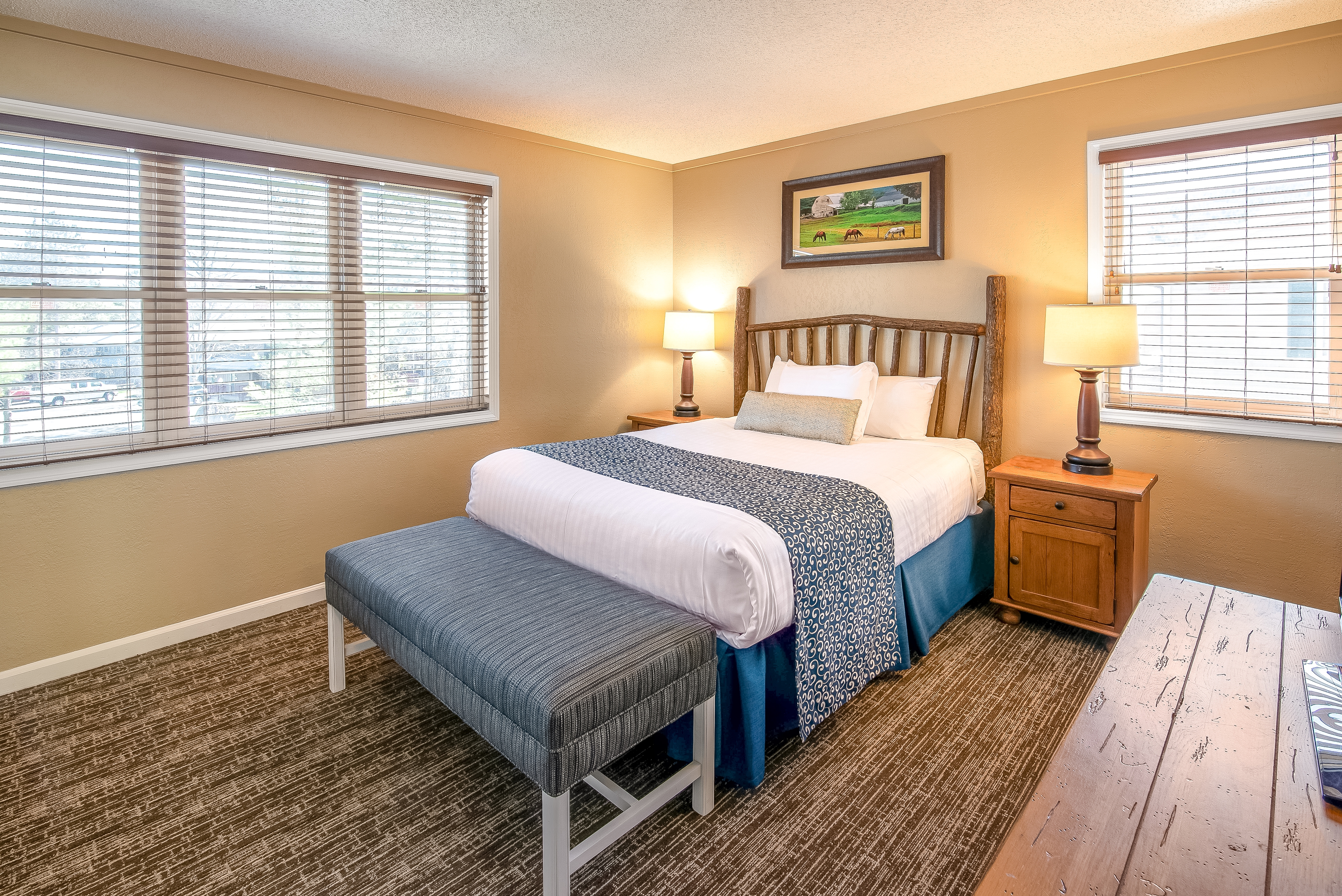 Bedroom with bench, end tables, and two large windows in a one bedroom villa at Oak n' Spruce Resort in South Lee, Massachusetts