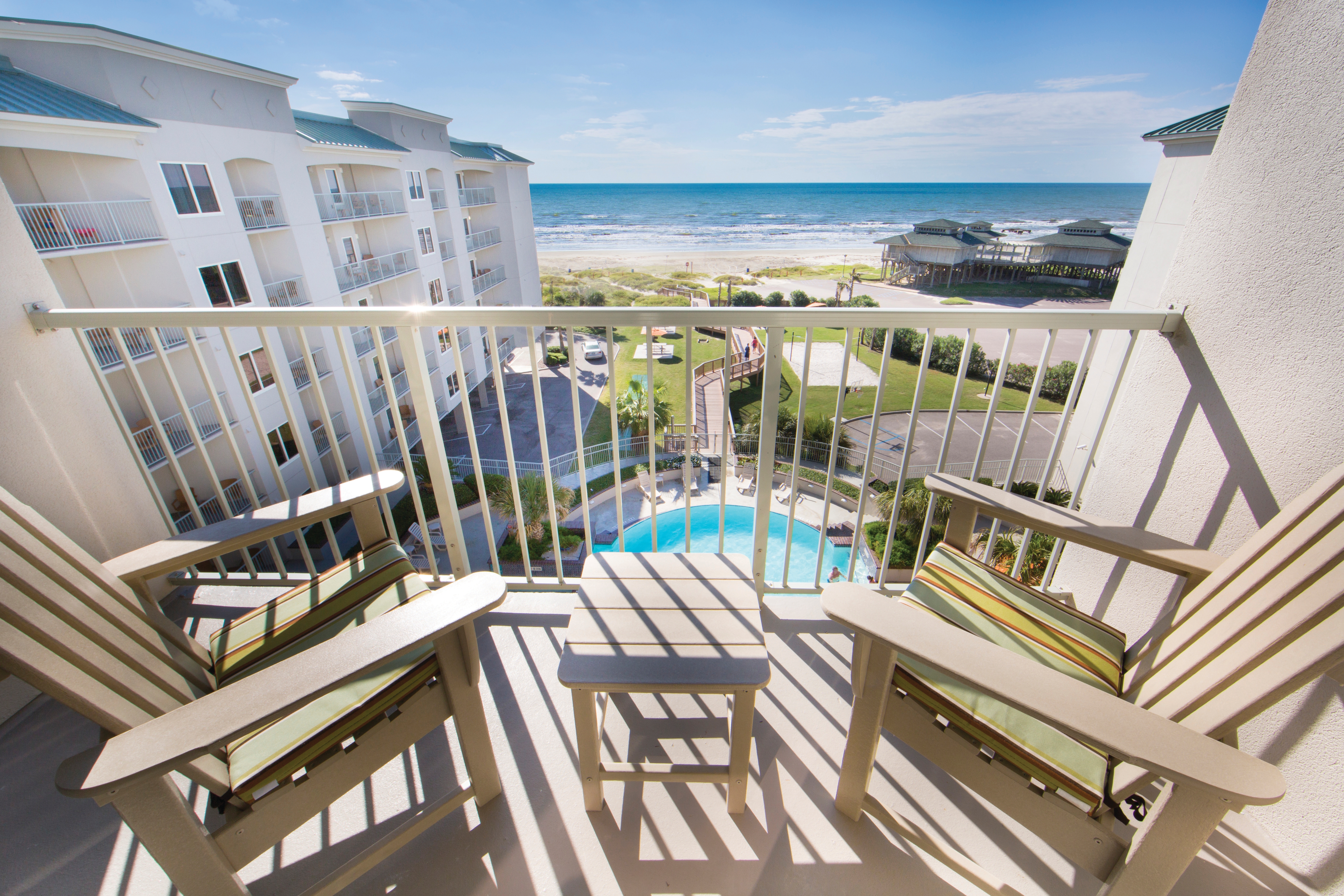 Balcony with two chairs overlooking the resort pool and beach in a Signature two-bedroom villa at Galveston Beach Resort