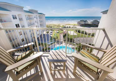 Balcony with two chairs overlooking the resort pool and beach in a Signature two-bedroom villa at Galveston Beach Resort