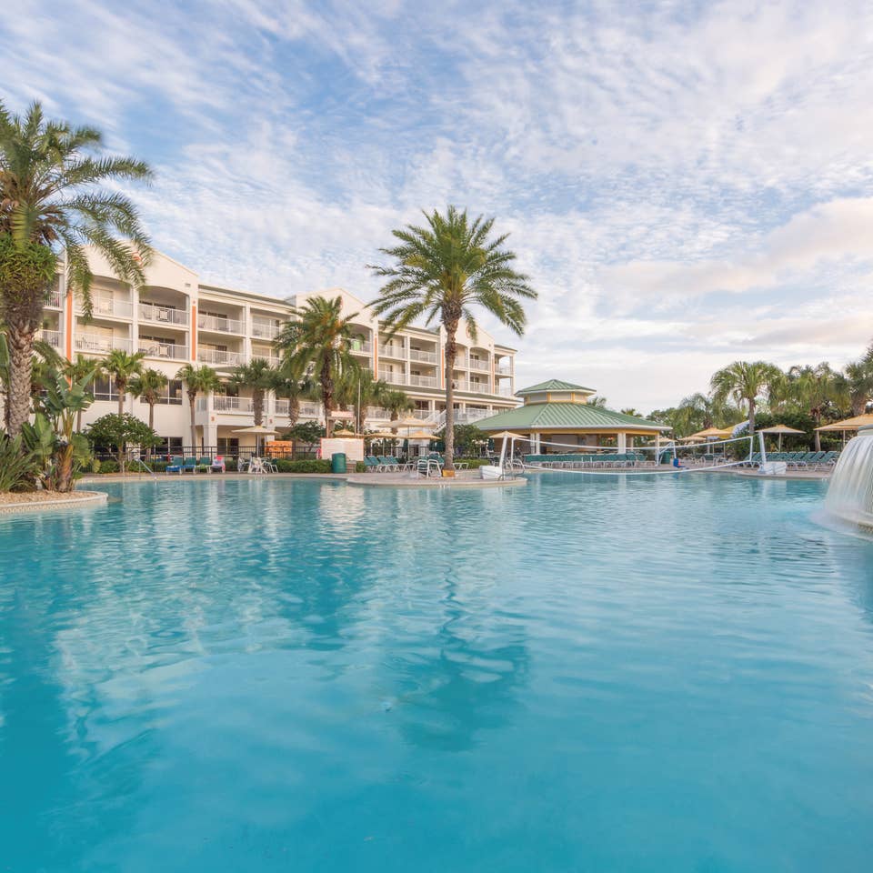 Outdoor pool with waterfall, volleyball net, beach chairs, and umbrellas at Cape Canaveral Beach Resort.