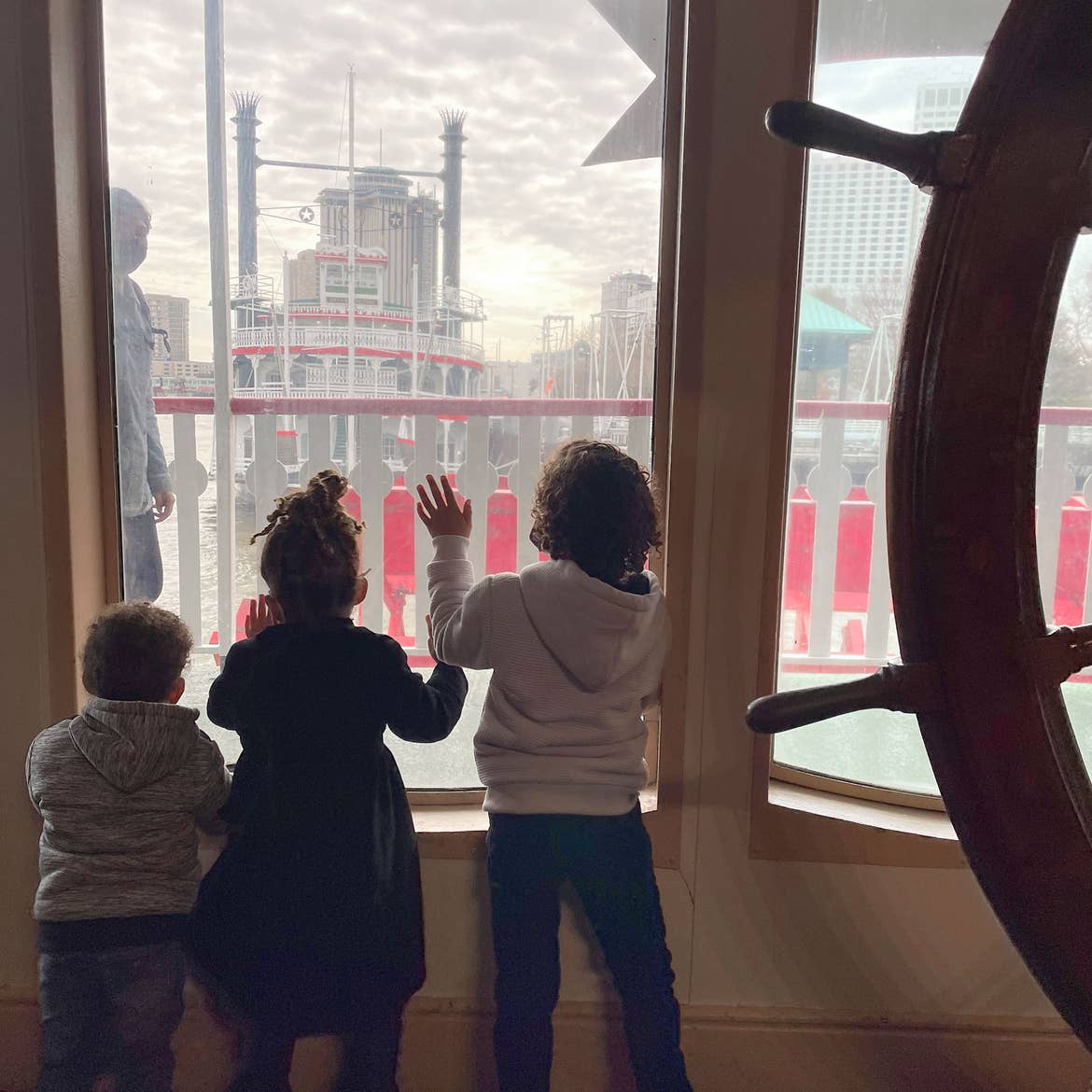 Featured Contributor, Sally Butan of @butanclan's children, Alston (left), Alissa (middle), and Alex (right) look out of a window on the Steamboat Natchez of the Mississippi River of New Orleans, Louisiana.