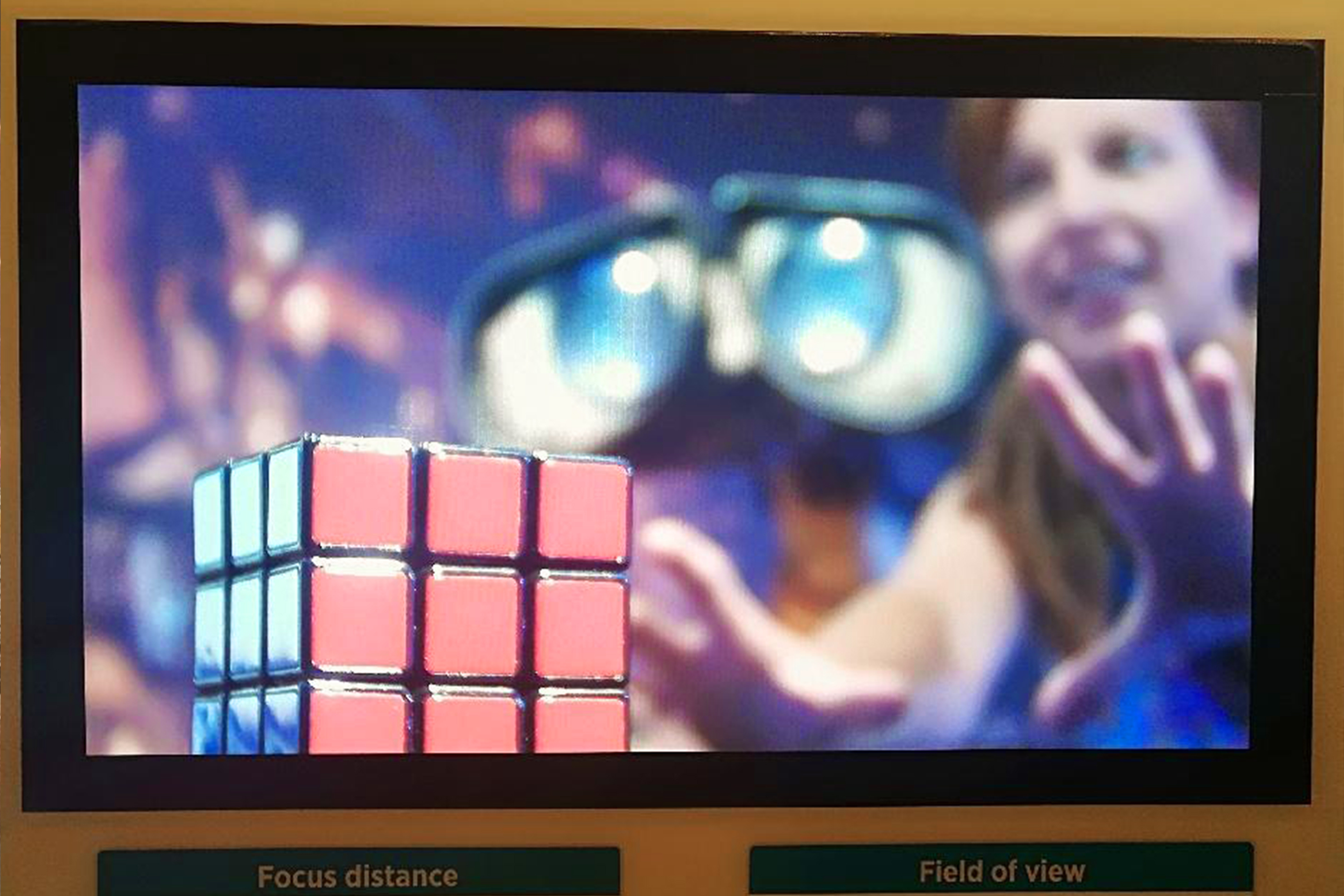 A monitor shows a woman standing next to Pixar's Wall-E reaching out for a Rubik's Cube.
