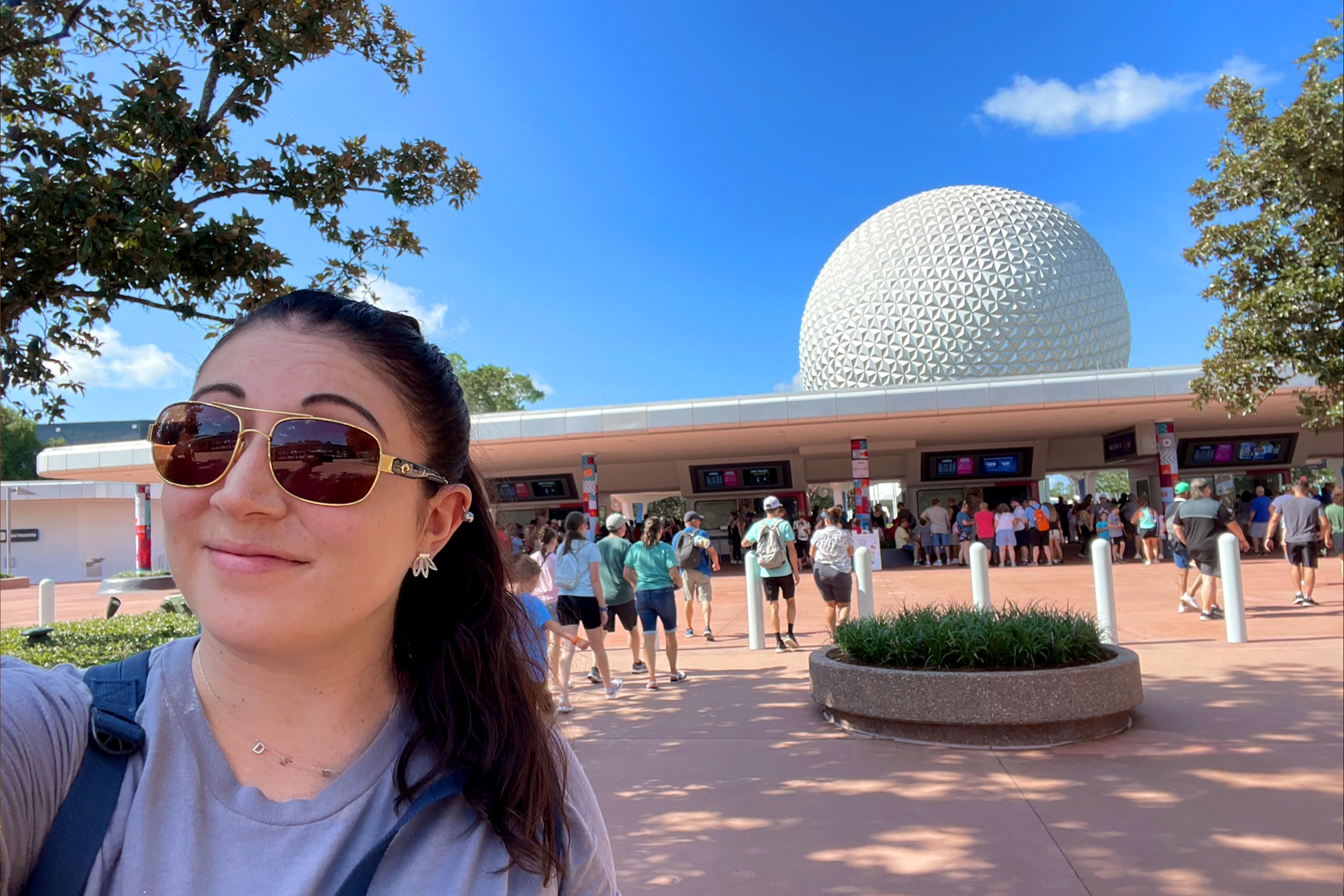 A woman wears sunglasses and t-shirt in front of the Epcot entrance.