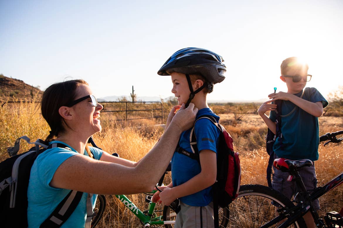 Author Jessica Averett (left) helps her son (middle) with his safety helmet as her other son (right) adjusts his Camelbak prior to riding bikes.
