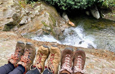 Featured Contributor, Jennifer C. Harmon (left) and her two girlfriends wear hiking boots as their feet sit near the top of a waterfall.