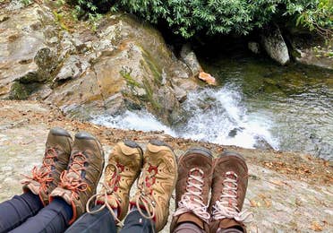 Featured Contributor, Jennifer C. Harmon (left) and her two girlfriends wear hiking boots as their feet sit near the top of a waterfall.
