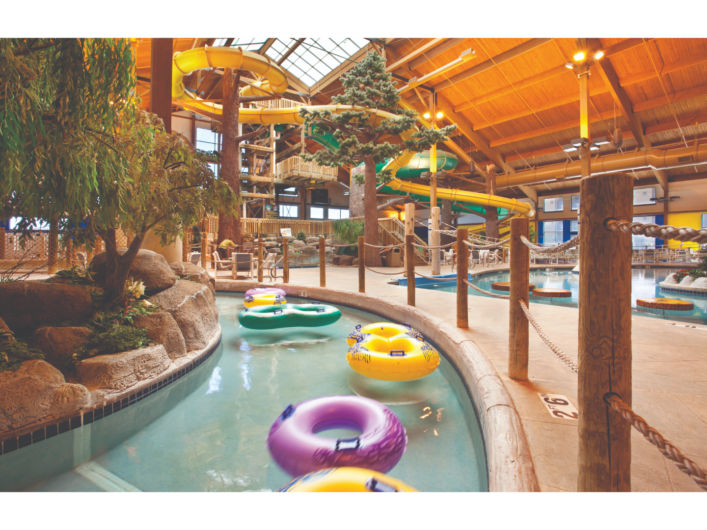 Indoor waterpark with slides, lazy river, trees, and cabin-style ceilings.