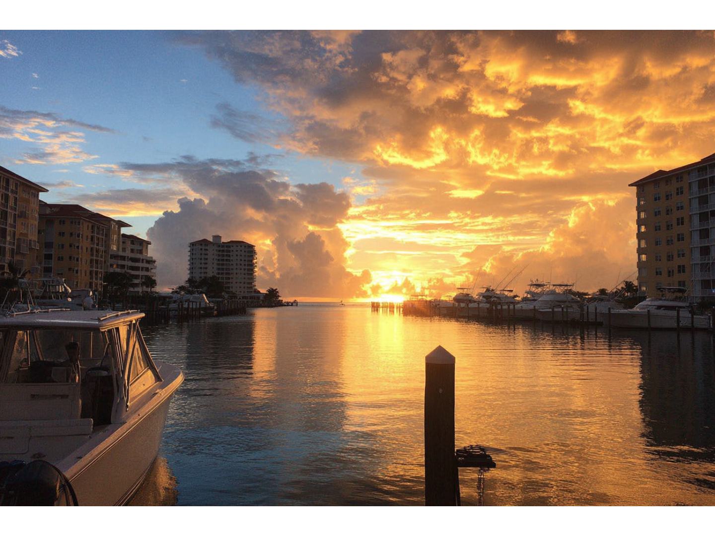 Golden sunset over marina with boats and waterfront buildings.