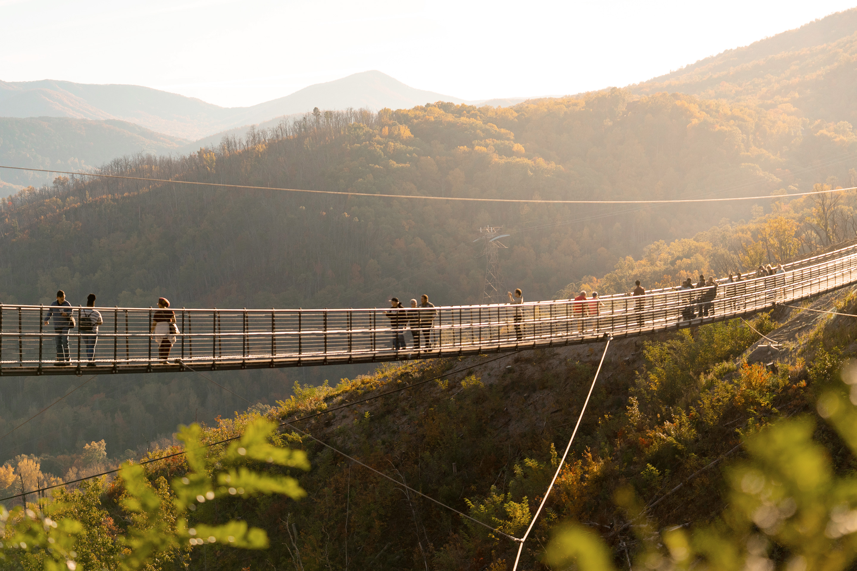 The Gatlinburg Sky Bridge hangs in front of a sunset as guests walk across the suspended bridge.