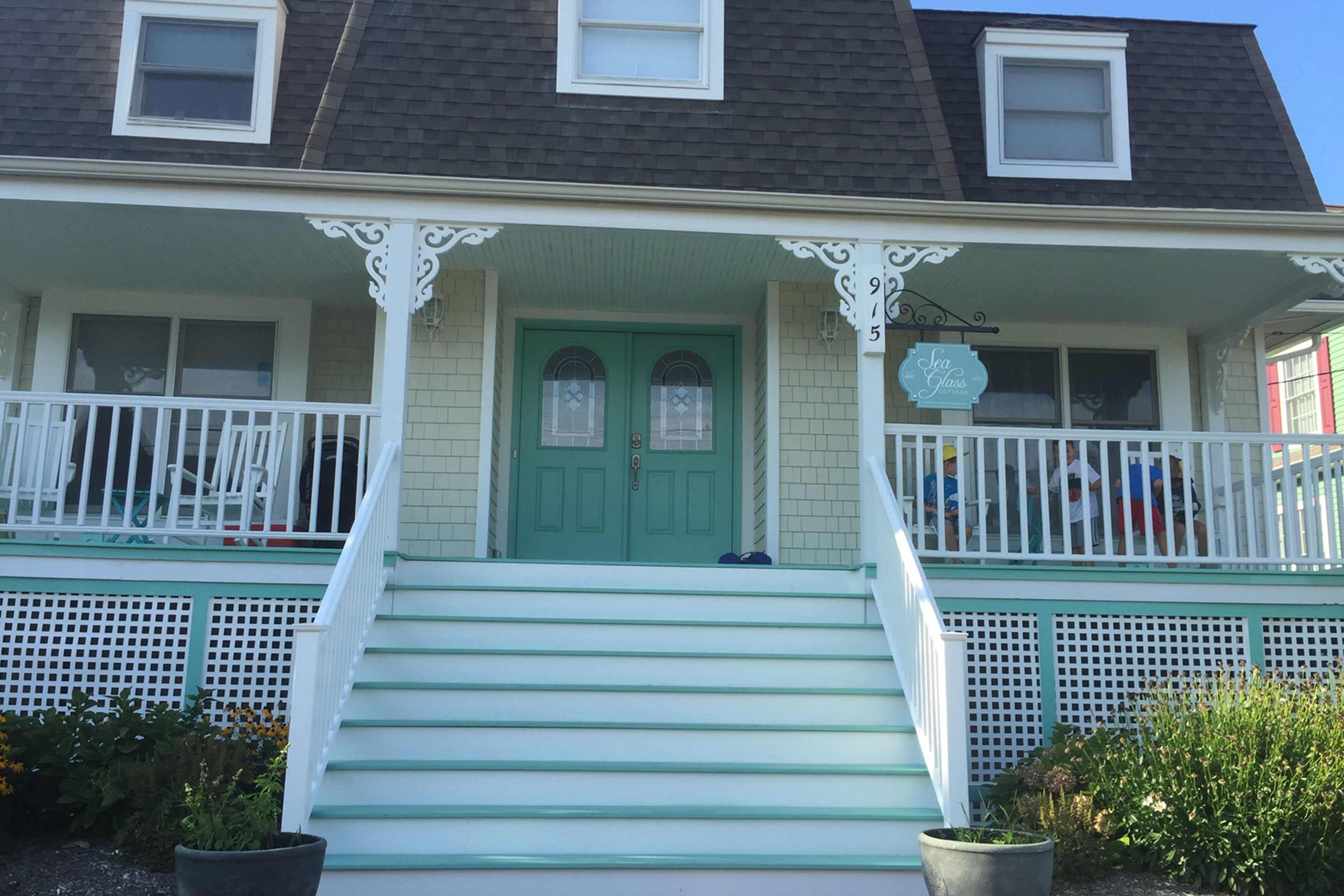 Exterior shot of the Sea Glass Cottage at Cape May with a wrap-around white porch and aqua siding and doors.