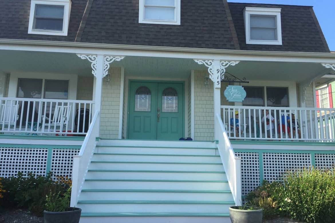 Exterior shot of the Sea Glass Cottage at Cape May with a wrap-around white porch and aqua siding and doors.