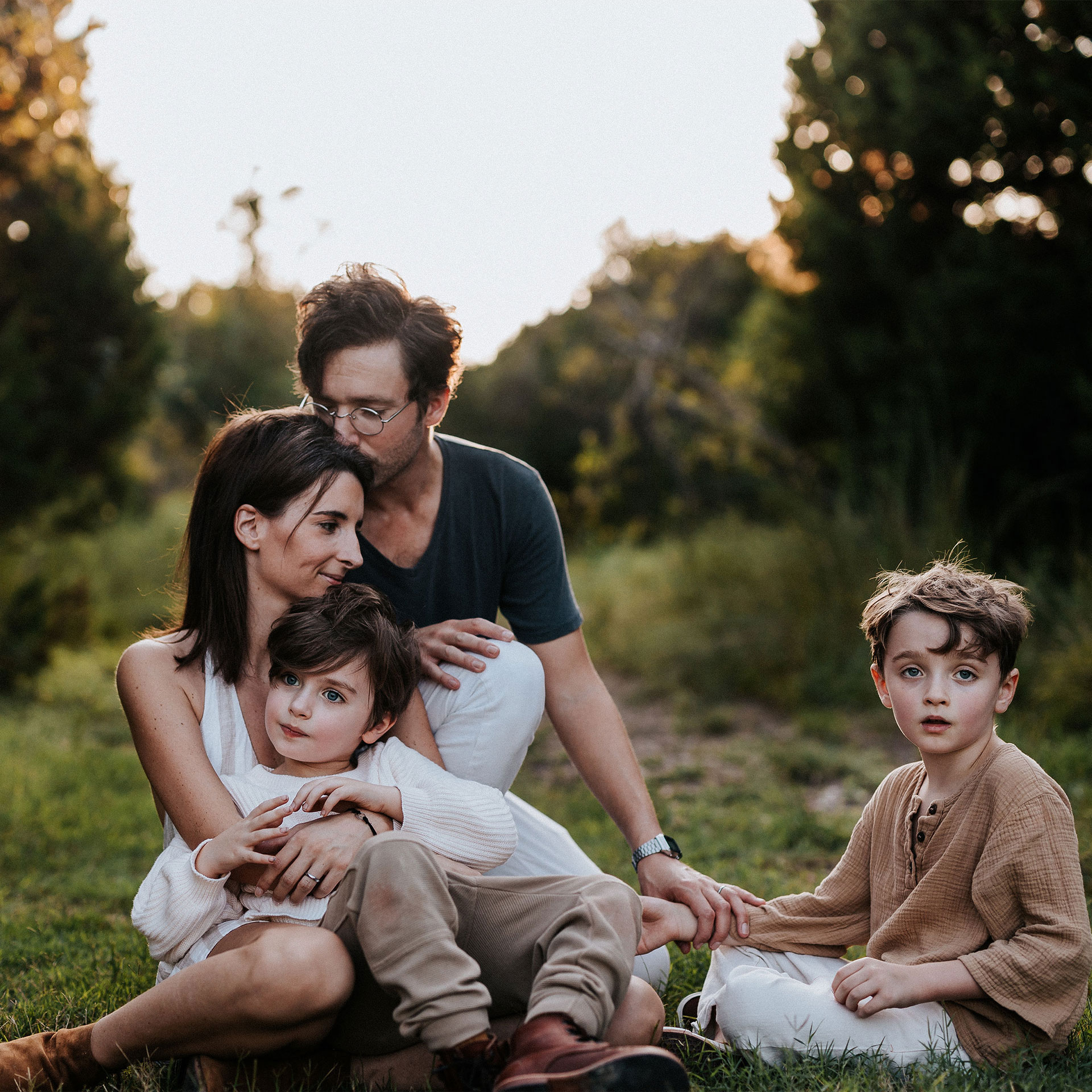 Featured Contributor, Eileen Lamb (middle-left), her husband (top-left) and sons, Jude (front-left) and Charlie (right) sit outdoors on the grass at dusk.
