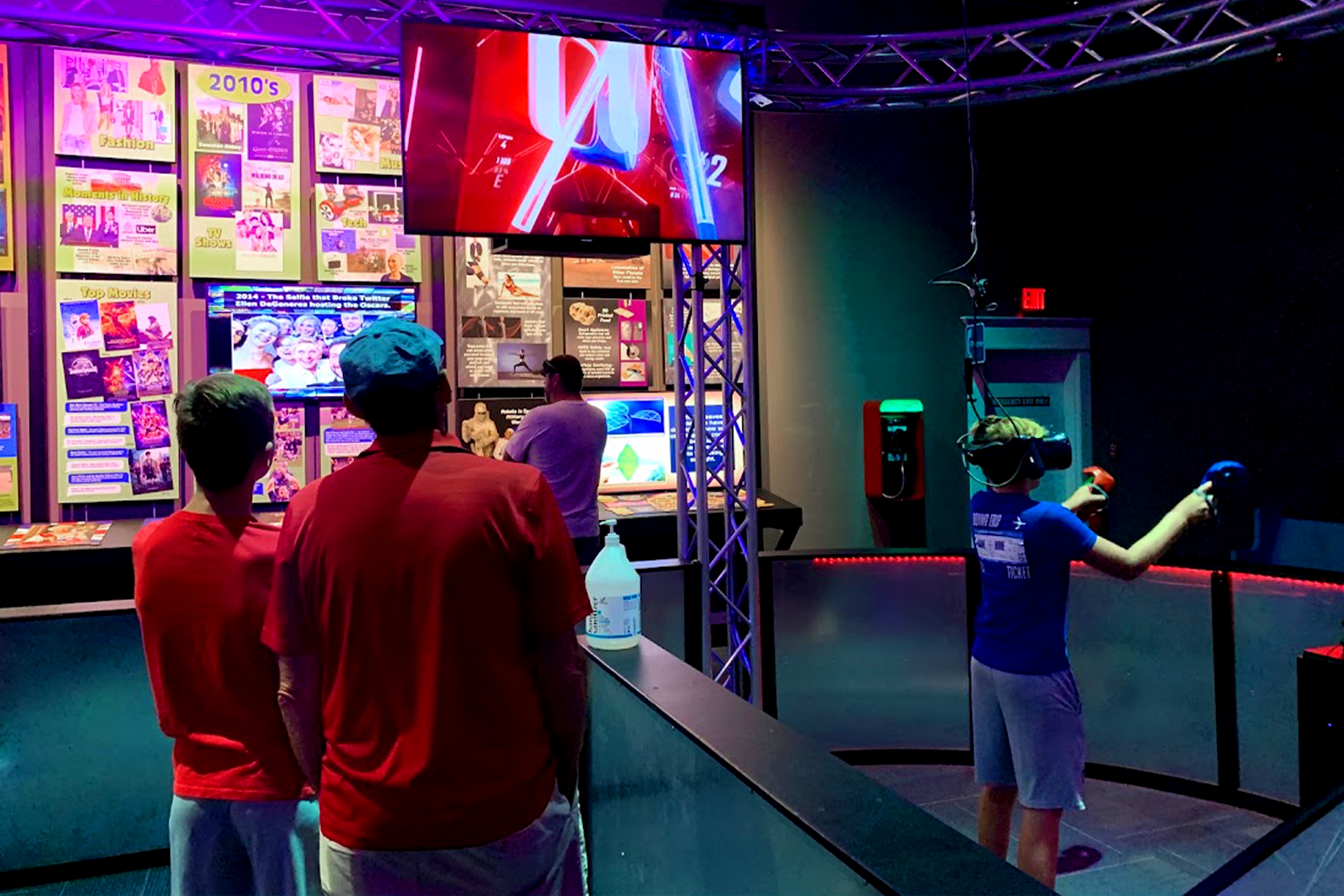 A boy plays a Virtual Reality game with accessories as a boy and man watch.