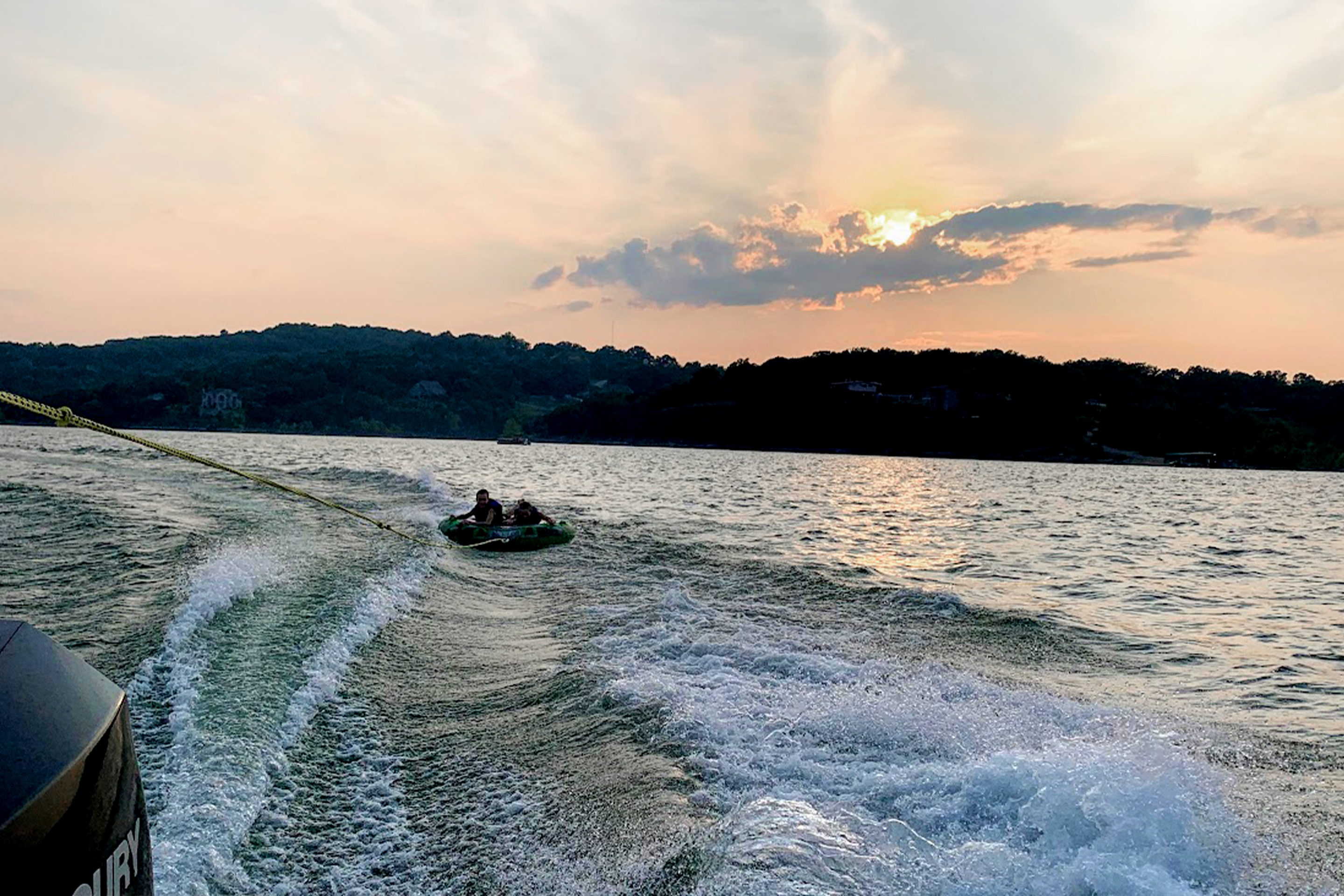 Two kids with lifejackets sit on a tube being towed by boat.