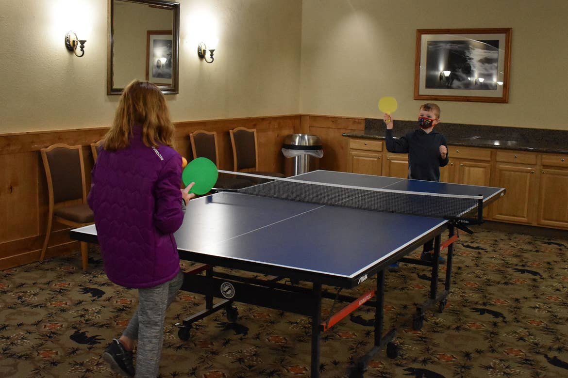 A young girl and boy play at an indoor ping table.