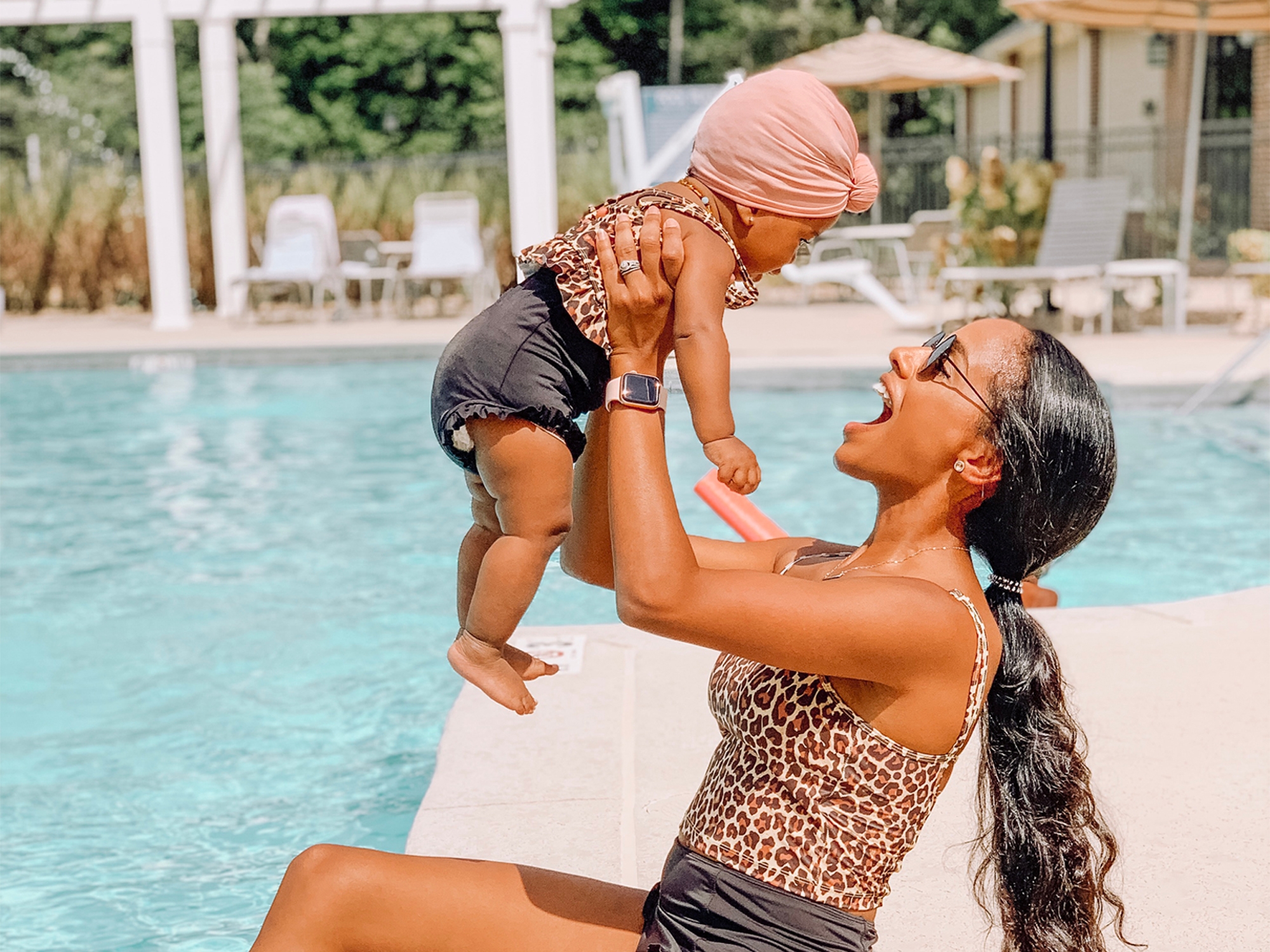 Aesky holding her baby in the air next to a pool