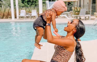 Aesky holding her baby in the air next to a pool