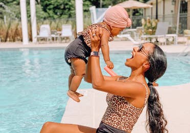 Aesky holding her baby in the air next to a pool
