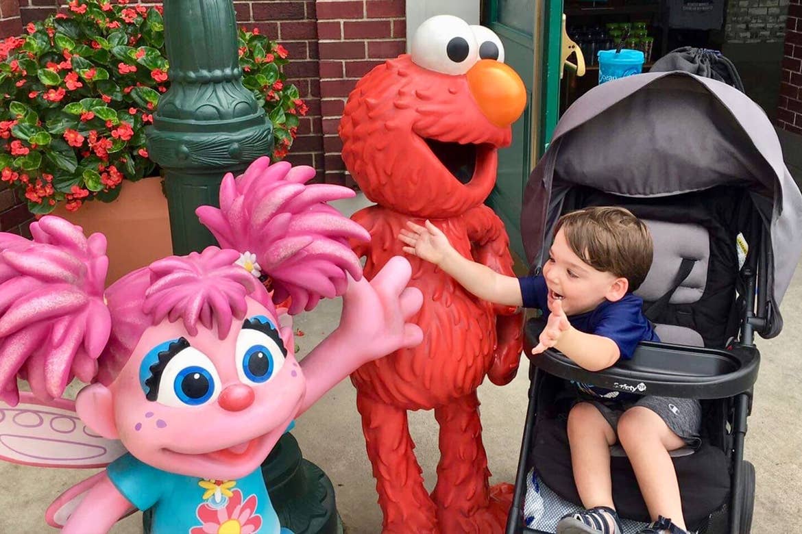 Dakota, Theresa's son, reaches from his stroller to embrace Elmo and Abby Cadabby outside Sesame Street Land.