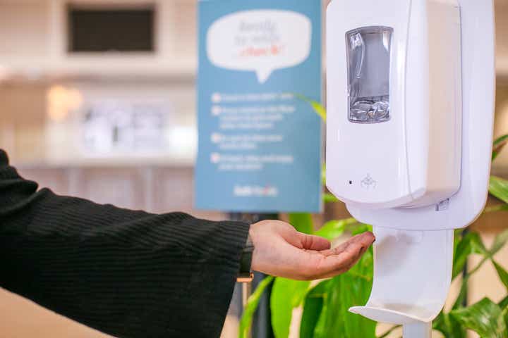 Hand reaching towards automatic hand sanitizer dispenser.