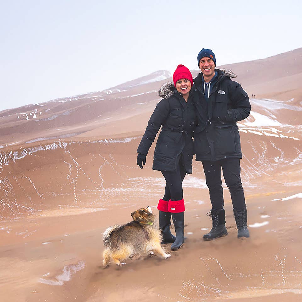 Authors, Lauren Layne and Anthony LeDonne, stand in winter apparel with Bailey the Pomeranian at the Great Sand Dunes National Park and Preserve.