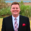 Chris Harms in a suit and tie with a lake and greenery in the background